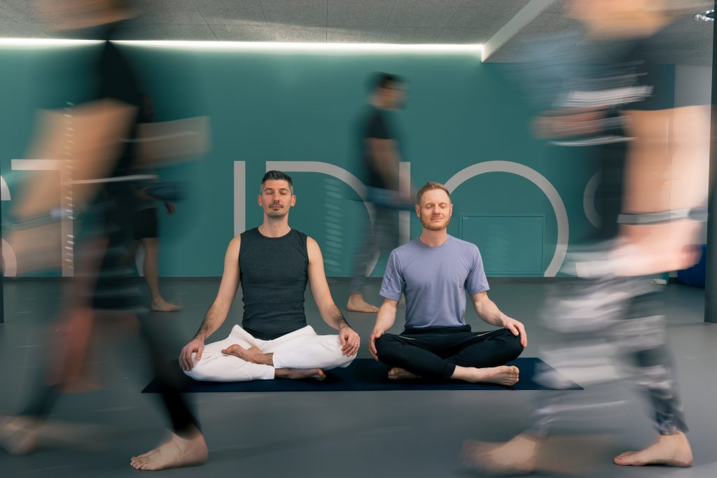 Chris and Vlad (Still and Strong Yoga founders) sitting in a meditation position depicting qualities of stillness and strength among 'chaos' and business around them.